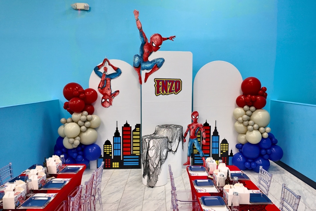 Spider-Man themed birthday party with custom cityscape backdrop and hanging superhero cutouts at Kidz Kastle RI