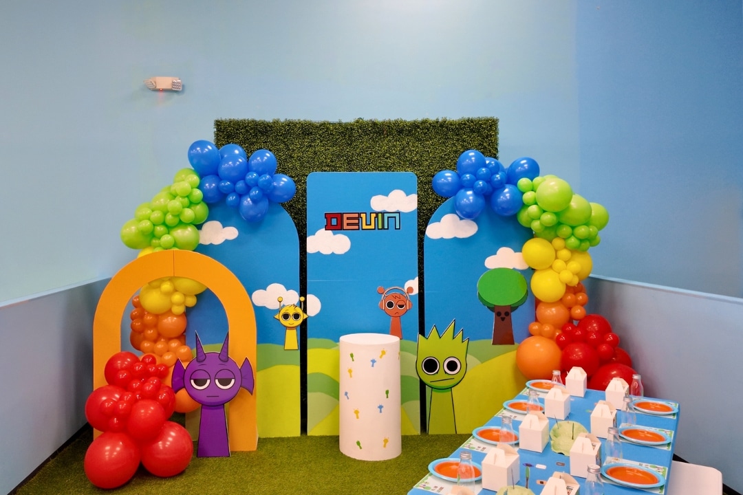 Sprunki themed kids birthday party for Devin with colorful character backdrop, rainbow balloon arch, and bright coordinated table setting at Kidz Kastle in Rhode Island.