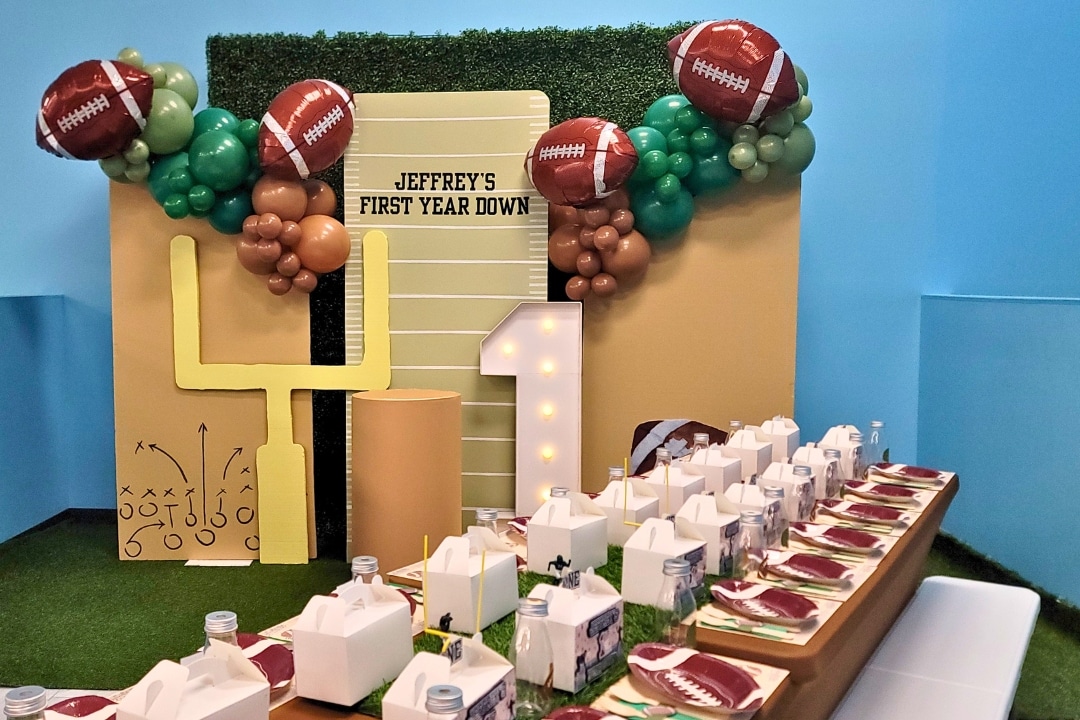 Custom "First Year Down" football themed first birthday party with goalpost backdrop and custom balloon decor at Kidz Kastle.