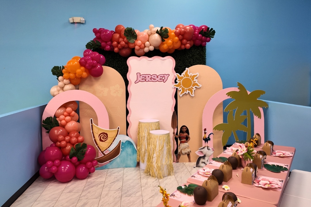 Custom Moana themed tropical luau party with a designer shimmer wall, hula-skirt pedestals, and custom balloon installations at Kidz Kastle.