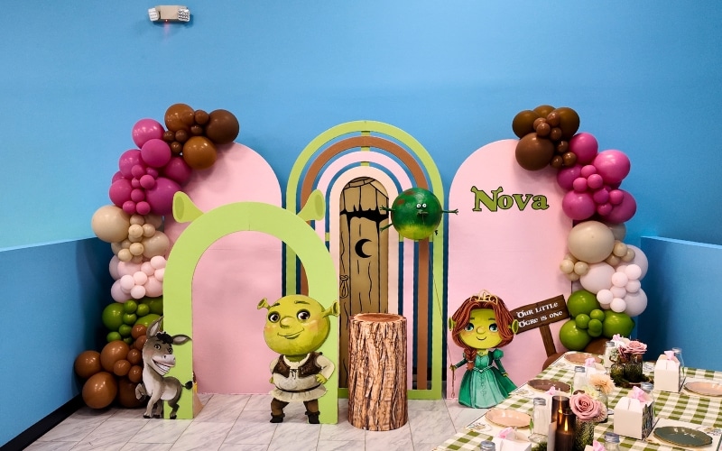 Custom Shrek themed first birthday party setup at Kidz Kastle private party venue in Warwick RI featuring balloon garlands character props and arch backdrop