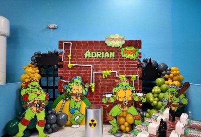 A custom Teenage Mutant Ninja Turtles themed setup for a private kids birthday party Warwick RI, featuring a brick backdrop, character cutouts, and themed balloon decor at Kidz Kastle.